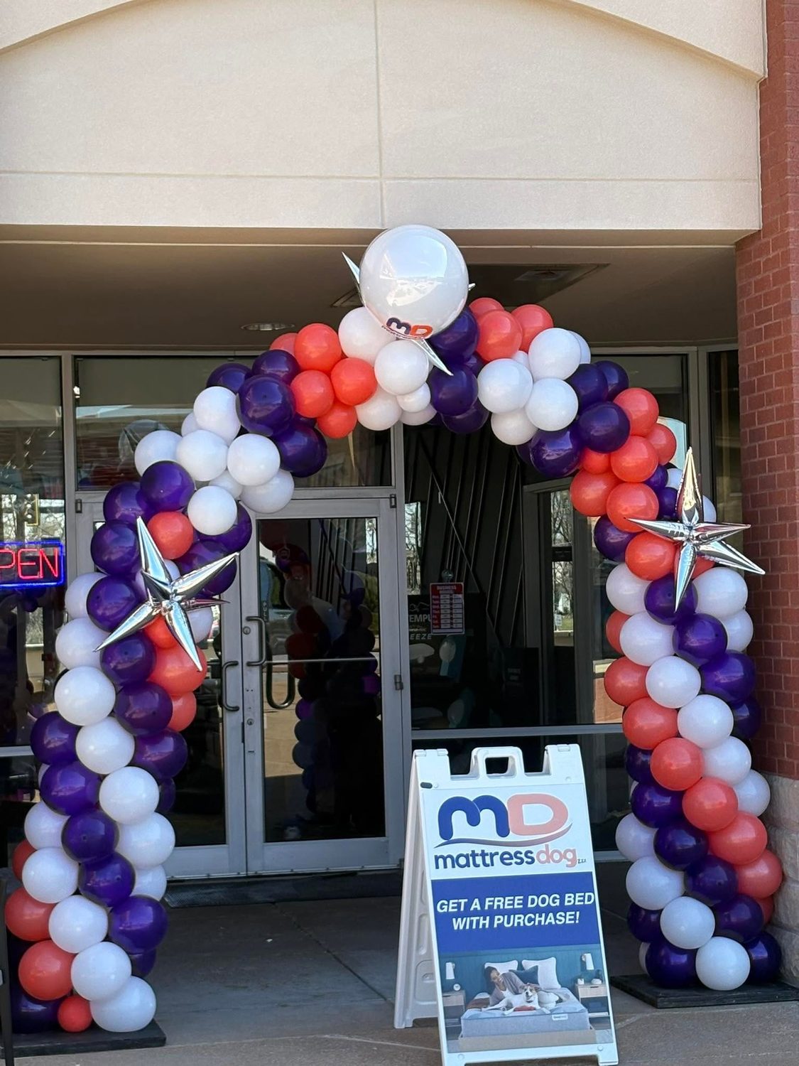 Corporate balloon entryway arch in purple coral and white with silver star balloons at a Mattress Dog storefront