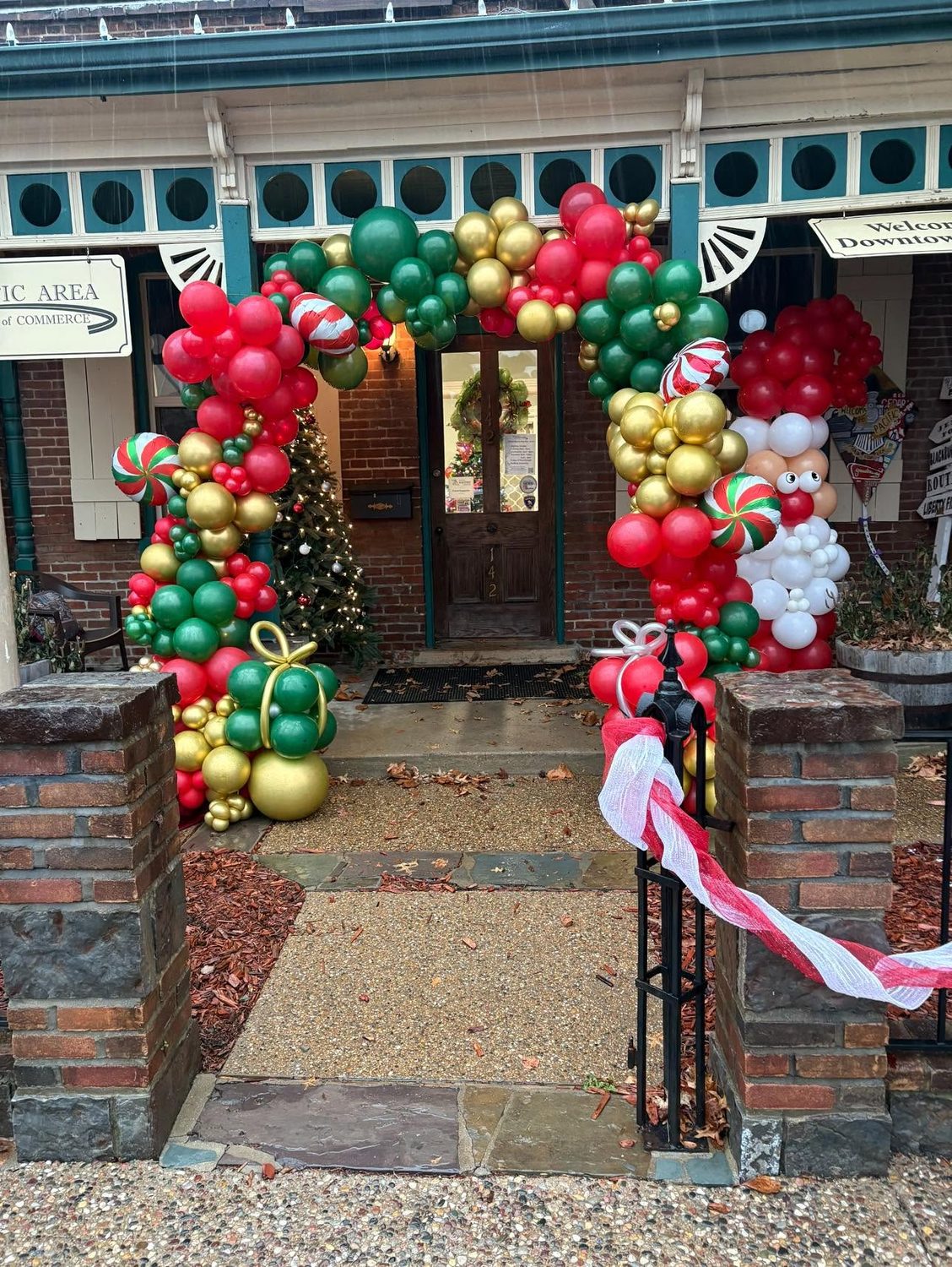Holiday balloon entryway arch in red green and gold with peppermint and snowman accents