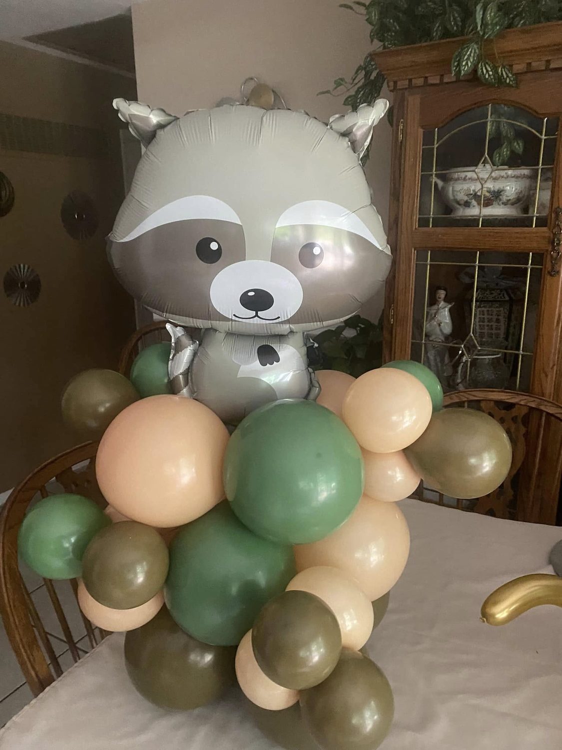 Raccoon balloon centerpiece in earth-toned green and tan balloons for a themed party